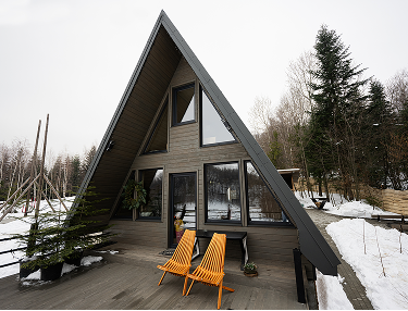 A-Frame-Haus mit Holzterrasse und orangen Stühlen im Schnee