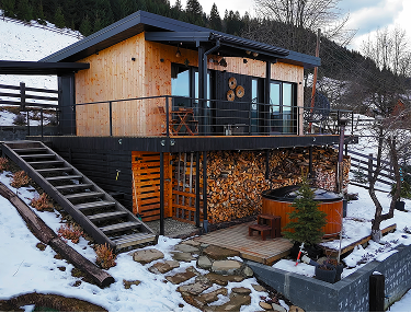 Holzhaus mit Balkon, Treppe und Badezuber am verschneiten Hang