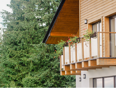 Holzbalkon mit Blumenkästen an einem Haus zwischen Tannen