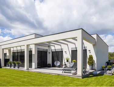 Weißer Bungalow mit Pergola und überdachter Terrasse am Rasen