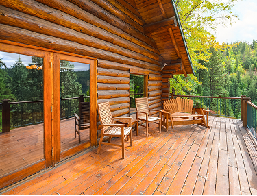 Holzterrasse eines Blockhauses mit Stühlen und Blick über den Wald