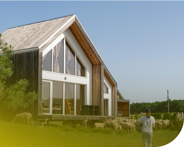 Ökohaus mit Holzfassade auf einer Weide, davor grasen Schafe