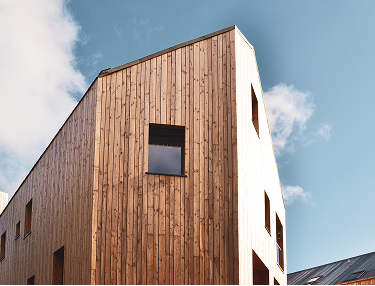 Haus mit Fassade aus senkrechten Holzlatten vor blauem Himmel