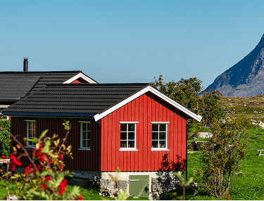 Rotes Holzhaus mit weißen Fenstern vor einem Berg