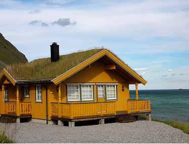 Gelbes Holzhaus mit Grasdach und Veranda am Meer