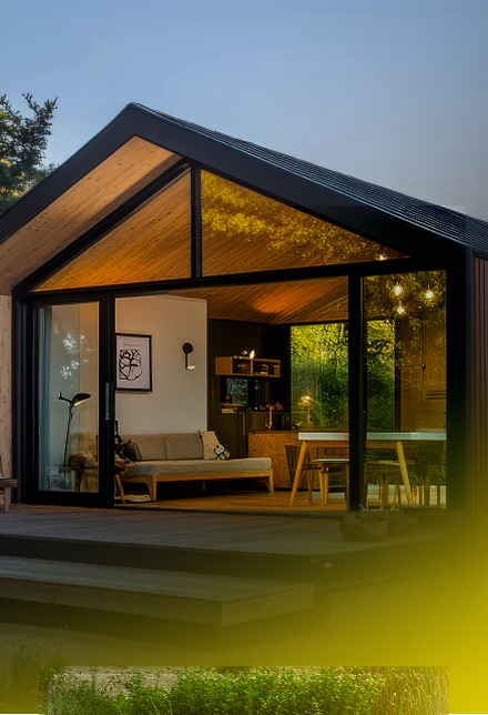 Modernes Tiny Haus aus Holz mit beleuchteter Glasfront in einem Waldgrundstück