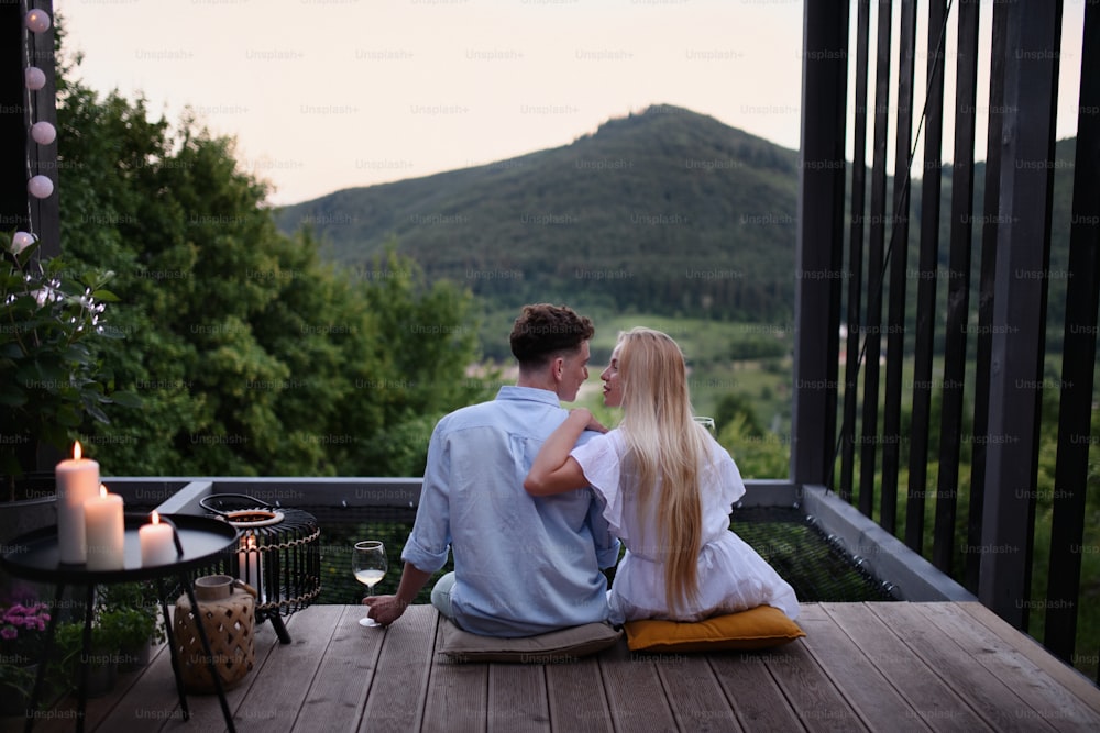 Ein junges Paar, das sich im Freien auf der Terrasse eines winzigen Hauses im Wald mit Blick am Abend ausruht, Wochenendausflug in einem winzigen Haus auf dem Land, nachhaltiges Leben.